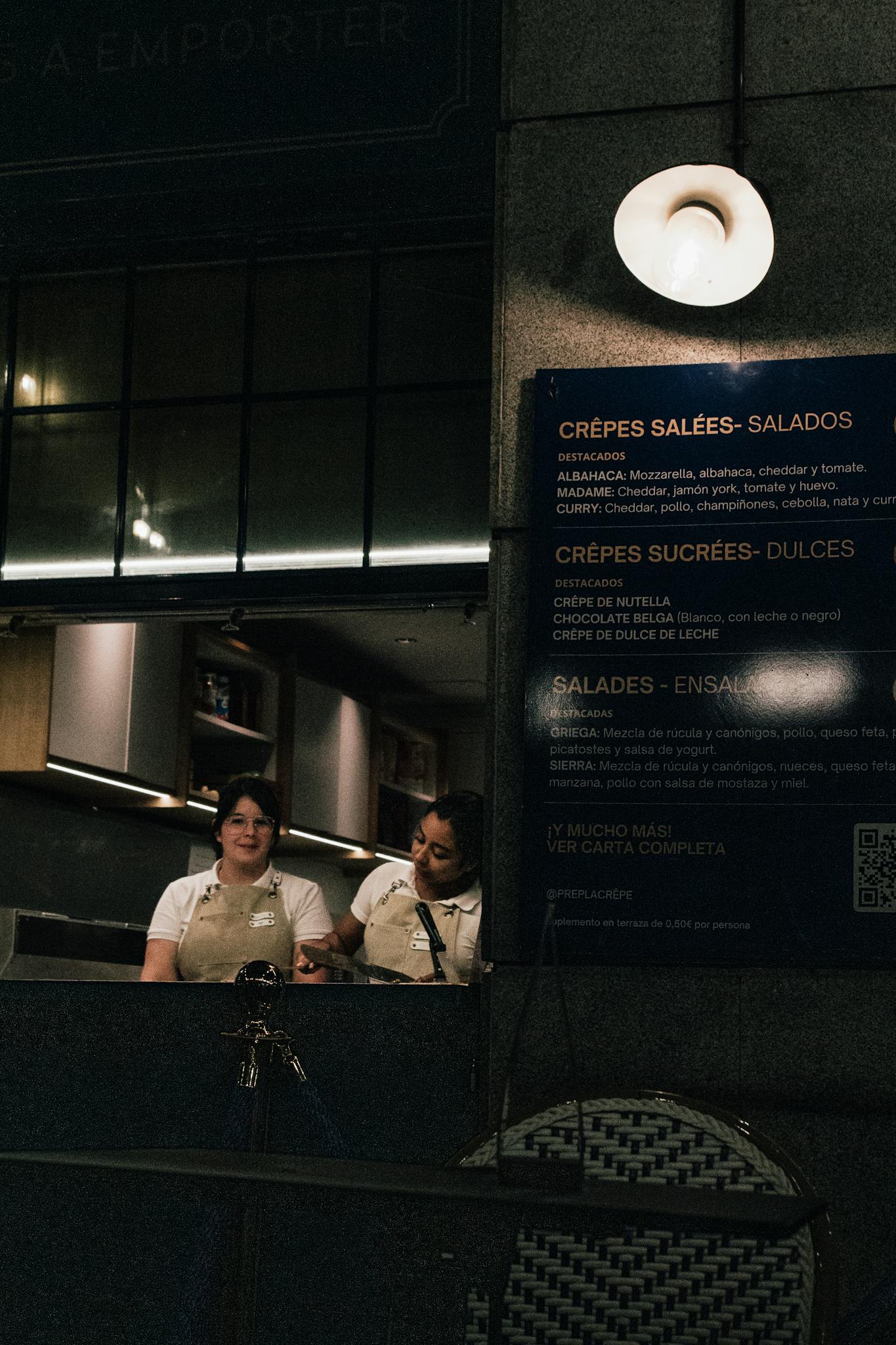 Nighttime cafe scene with two female staff preparing in a warm, ambient setting.